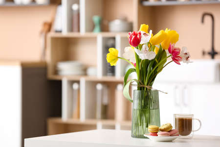 Vase with beautiful flowers and tasty breakfast on dining table in kitchen