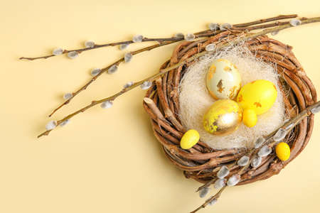 Nest with painted Easter eggs and pussy willow branches on color backgroundの写真素材