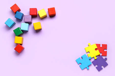 Frame made of wooden cubes and puzzle pieces on lilac background