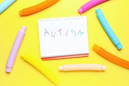 Notebook with word AUTISM and Pop Tubes on yellow background
