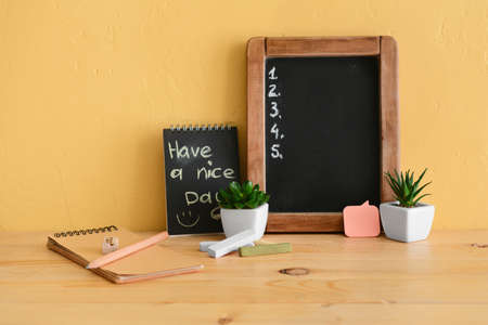 Chalkboard with empty to-do list, pen and notebook with text HAVE A NICE DAY on table near yellow wallの写真素材