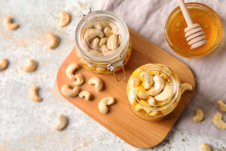 Board with jars of sweet cashew nuts in honey on grunge background