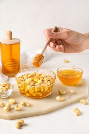 Female hand with dipper and sweet cashew nuts in honey on light backgroundの写真素材