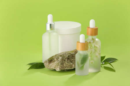 Bottles of natural serum, stone and plant leaves on green background