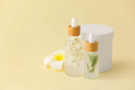 Bottles of natural serum with flower on yellow background