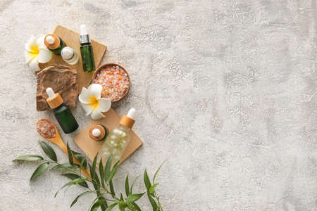 Composition with bottles of natural serum, salt and flowers on light grunge background