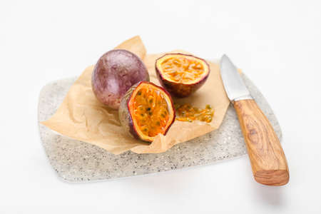 Board with delicious passion fruit and knife on white background