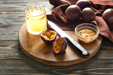 Glass of juice and board with delicious passion fruits on wooden background