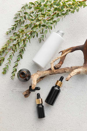 Bottles of natural serum, tree branch and plant leaves on light backgroundの写真素材
