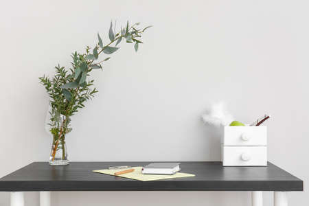 Modern desk with plant branches in vase and drawers near light wallの写真素材