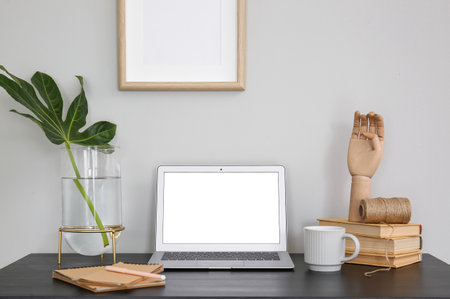 Laptop with plant leaf in vase, wooden hand and cup on table near white wallの写真素材