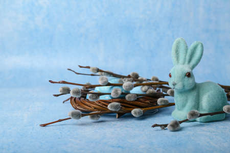 Willow branches, nest with painted eggs and Easter bunny on blue background