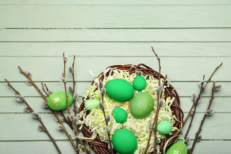 Willow branches and nest with painted Easter eggs on green wooden backgroundの写真素材