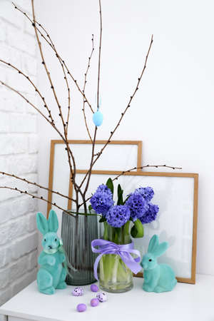 Easter eggs, bunnies and hyacinth flowers on chest of drawers near white wall