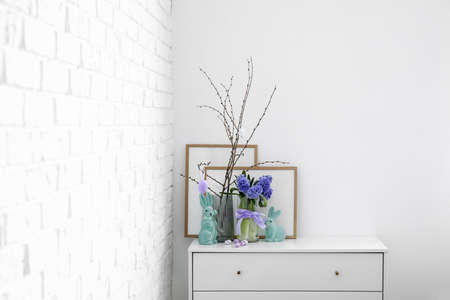 Easter eggs, bunnies and hyacinth flowers on chest of drawers near white wall