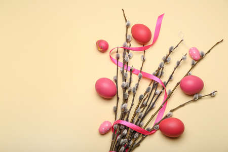 Willow branches, ribbon and painted Easter eggs on yellow background