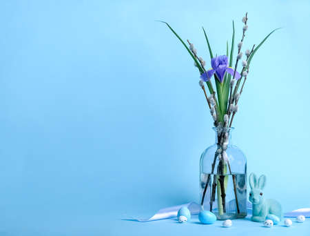 Vase with willow branches, flower, bunny and painted Easter eggs on blue backgroundの写真素材