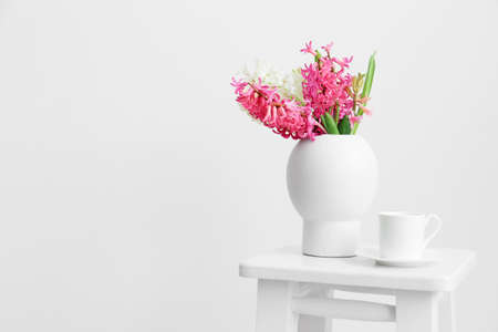 Vase with hyacinth flowers and cup on stool near white wallの写真素材