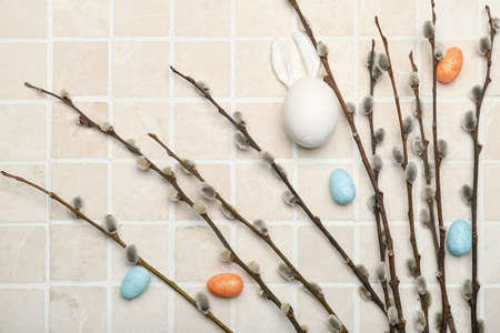Willow branches and painted Easter eggs on light tile background