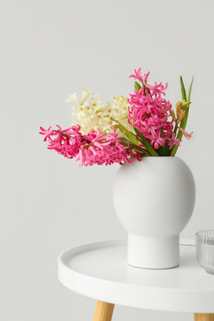 Vase with hyacinth flowers and candle on table near white wallの写真素材