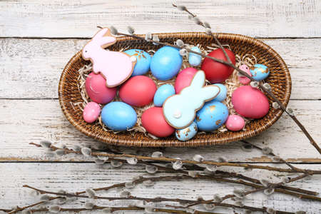 Willow branches, Easter cookies and basket with painted eggs on light wooden background