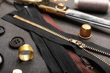 Set of stylish zippers and sewing supplies on dark background