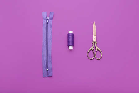 Stylish zipper, thread and scissors on purple background