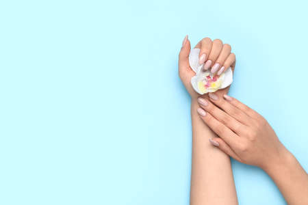 Woman with beautiful manicure holding orchid flower on blue background, closeupの写真素材