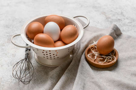 Colander with fresh chicken eggs and whisk on light backgroundの写真素材
