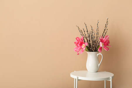 Jug with pussy willow branches and tulip flowers on table near beige wallの写真素材