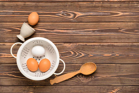 Colander with fresh chicken eggs on wooden background