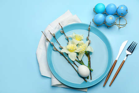 Plate with beautiful daffodils flowers, pussy willow branches and painted Easter eggs on blue backgroundの写真素材