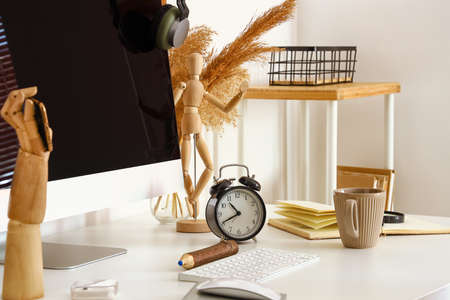 Modern computer, alarm clock and stylish decor on table near light wall, closeup