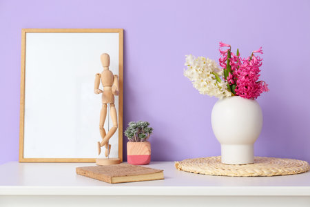 Blank photo frame, wooden mannequin doll, houseplant and vase with hyacinth flowers on table near color wallの写真素材