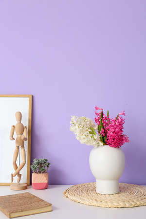 Vase with hyacinth flowers, notebook, houseplant and wooden mannequin doll on table near color wallの写真素材