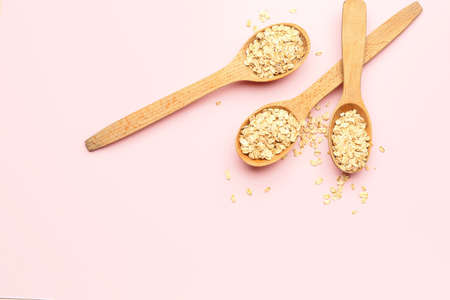 Wooden spoons with raw oatmeal on pink background