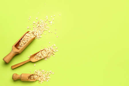 Wooden scoops with raw oatmeal on green background