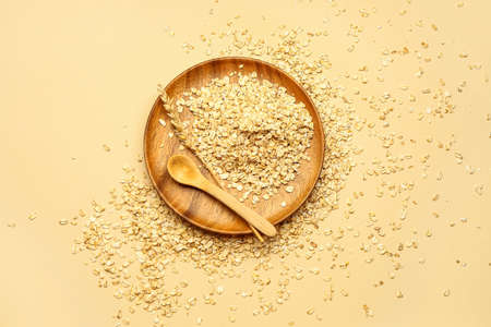 Plate of raw oatmeal and spoon on color background
