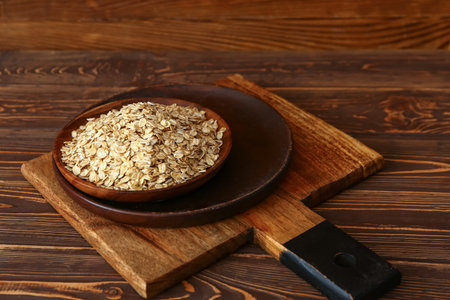 Board with plate of raw oatmeal on wooden background