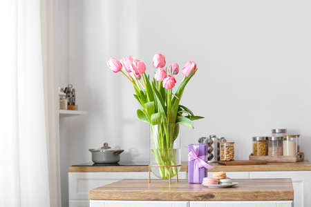 Vase with tulips, gift box and macarons on table in light kitchenの写真素材