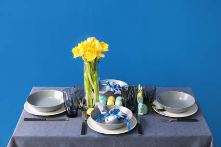 Table with beautiful setting served for Easter celebration near blue wall