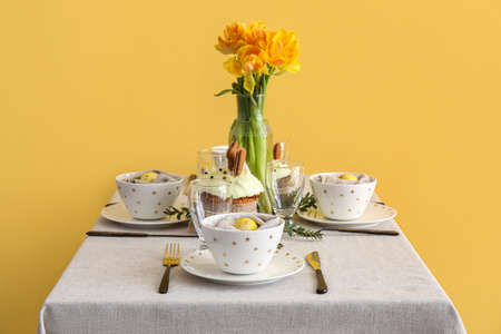 Table with beautiful setting served for Easter celebration near yellow wall