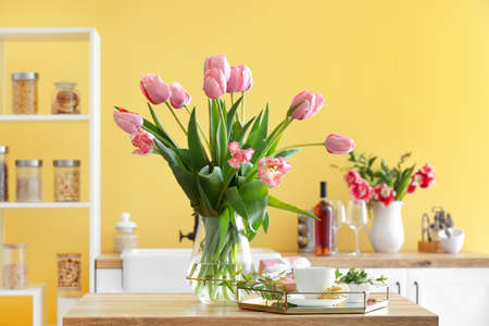 Vase with tulips, gift box, cup of coffee and macarons on table in kitchenの写真素材