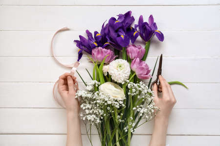 Female hands with beautiful flowers, scissors and ribbon on light wooden backgroundの写真素材