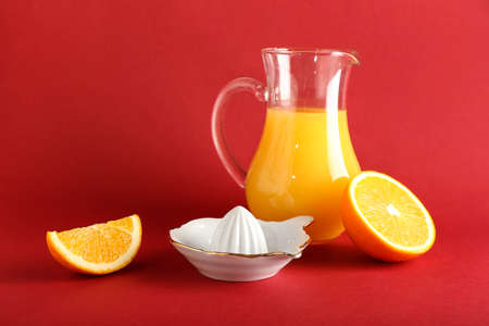 Ceramic juicer, jug of juice and orange on red backgroundの写真素材