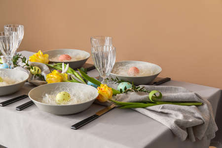 Stylish table setting with Easter eggs and floral decor near color wall