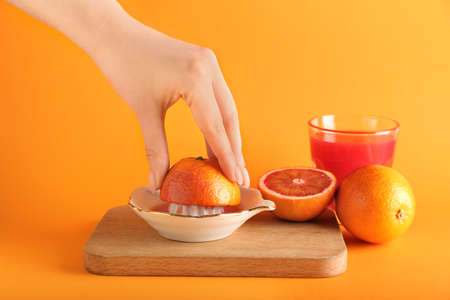 Woman squeezing fresh orange on orange background