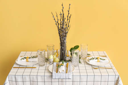 Vase with pussy willow branches on table served for Easter celebration near yellow wallの写真素材