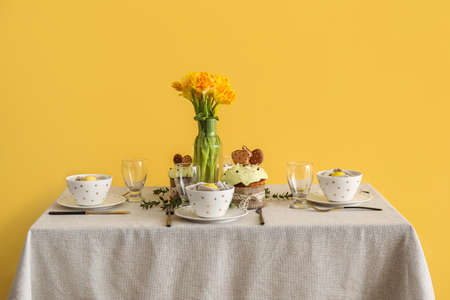 Table with beautiful setting served for Easter celebration near yellow wall