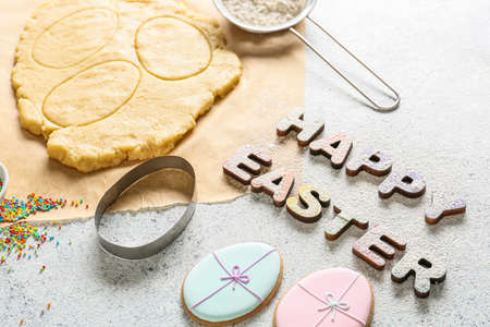 Text HAPPY EASTER made of wooden letters and tasty cookies on light background